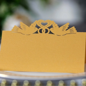 Laser cut hollow wedding place cards with heart and bird design in gold pearlescent paper
