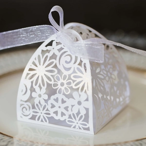 Macro view of white laser-cut pearl paper candy box with silver ribbon on a porcelain plate