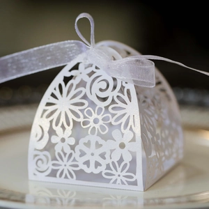 Close-up of laser-cut hollow floral pattern on white wedding favor box with ribbon