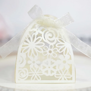 Macro detail of laser-cut floral patterns on cream paper wedding gift box with organza bow