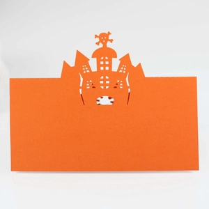 Macro detail of laser-cut orange Halloween table card with hollow castle and skull design