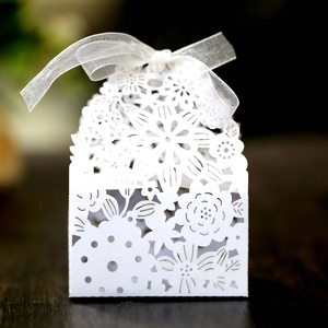 Close-up of white laser-cut wedding favor box featuring floral patterns and a silk ribbon