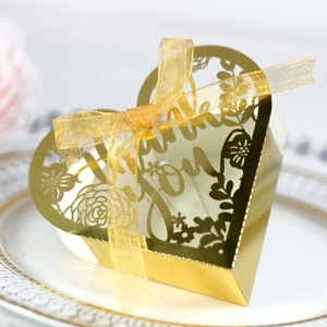 Detail of laser-cut heart candy box with Thank You text and golden ribbon on a porcelain plate