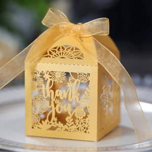 Macro view of gold laser-cut 'Thank You' favor box with pearl texture and chiffon ribbon