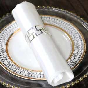 Close-up of geometric hollow silver napkin ring on white silk napkin for elegant table setting