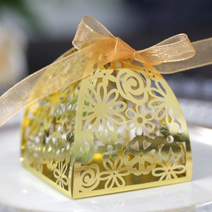 Detail of laser-cut gold wedding favor box with intricate floral patterns and organza ribbon