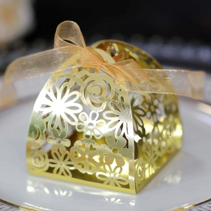 Detail of laser-cut gold wedding favor box with floral patterns and satin ribbon bow
