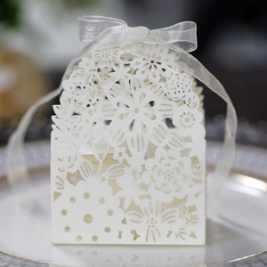 Macro detail of laser-cut cream wedding candy box with elegant floral patterns and ribbon