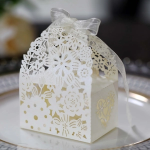 Close-up of laser-cut wedding favor box with floral patterns and a white ribbon bow