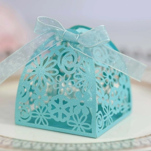 Close-up of laser-cut wedding candy box with floral patterns and light blue ribbon bow
