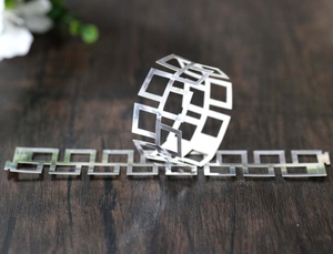 Detail of silver geometric cut-out metal napkin ring and strip on a wooden background