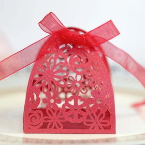 Macro shot of laser-cut floral patterns and red ribbon bow on a wedding candy box