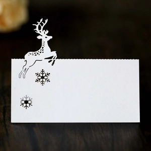 Elegant white laser-cut reindeer and snowflake place card on dark wooden surface