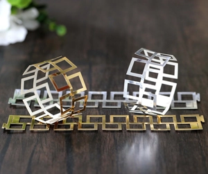 Macro detail of gold and silver hollow square pattern napkin rings on dark wood