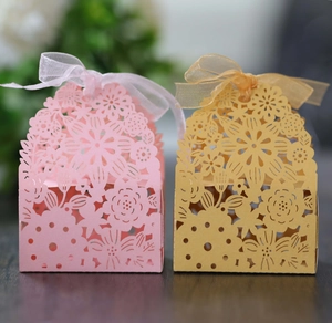 Detail of laser-cut floral wedding candy boxes with pink and gold ribbons
