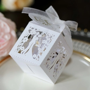 Detail of laser-cut ivory wedding favor box with bride and groom pattern and ribbon