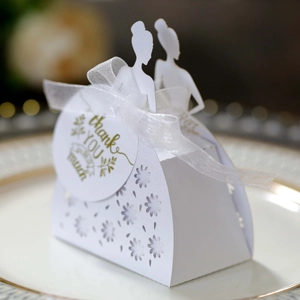Detail of white laser-cut wedding favor box with ribbon and Thank You tag on a plate