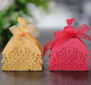 Detail of laser-cut wedding favor boxes in dress shape with red and gold hollow floral patterns