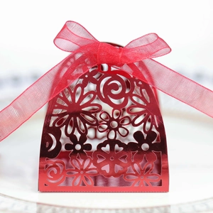 Macro shot of laser-cut red hollow wedding candy box with floral patterns and a silk ribbon