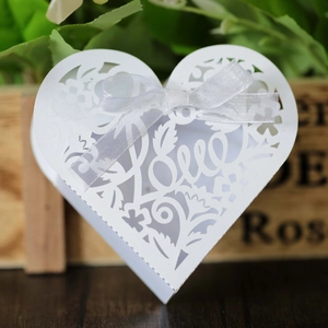 Detail of white heart-shaped wedding favor box with laser-cut Love pattern and bow