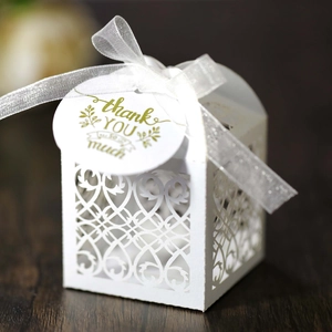 Detail of white laser-cut wedding favor box with ribbon and gold foil thank you tag