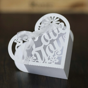 Detail view of white heart-shaped wedding favor box with Love You laser-cut design and bow