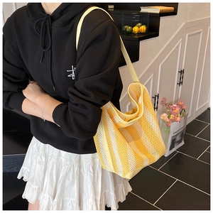 Détail d'un sac cabas en maille rayée jaune et blanc porté à l'épaule