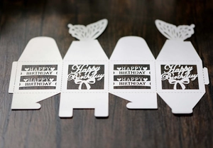 Flat lay of white laser-cut birthday favor box with butterfly handle on wood background