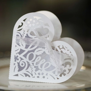 Detail of white heart-shaped favor box with laser-cut Love text and silk ribbon bow