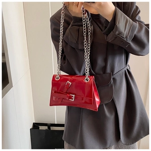 Detail of red patent leather crossbody bag with silver chains worn by model