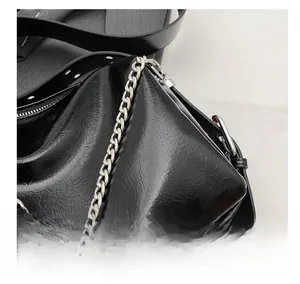 Detail of glossy black leather handbag showing silver chain and soft pleated texture