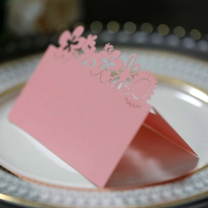 Detail of pink laser-cut flower table card on ceramic plate for wedding events