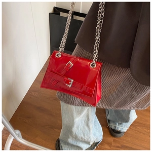 Detail of red patent leather crossbody bag with silver chains and buckle straps