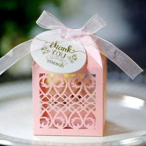 Detail of pink laser-cut wedding candy box with white silk bow and thank you tag