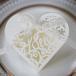 Close-up of white heart-shaped laser cut wedding favors box with Love lettering and ribbon