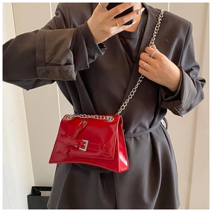 Detailed view of red patent leather crossbody bag with silver chains and buckle straps