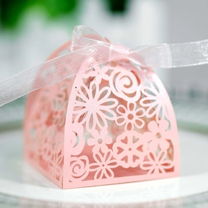 Detailed laser-cut floral pattern on light pink candy box with silver ribbon on a plate