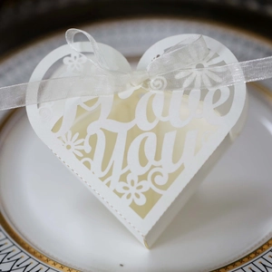 Macro shot of white heart-shaped favor box with laser-cut Love You text and satin ribbon