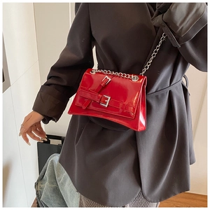 Macro detail of glossy red patent leather crossbody bag with silver metal chain strap