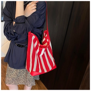 Detail view of red and white striped mesh tote bag with wide shoulder strap on model