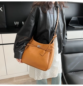 Detail of tan bucket bag with metal buckle and leather tag worn with a black jacket