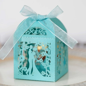 Macro detail of laser-cut wedding candy box with bride groom pattern and blue ribbon