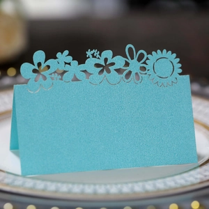 Laser-cut light blue place card with floral patterns on an elegant dinner plate