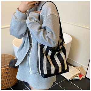 Detail of black and white striped mesh tote bag with leather straps on a shoulder