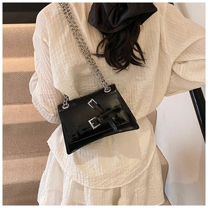Detail of a chic black shoulder bag with silver buckles and metal chain strap on model