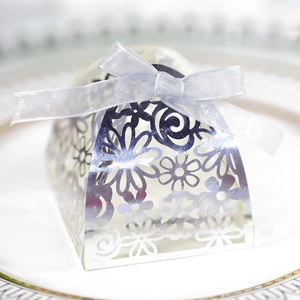 Macro shot of silver laser-cut wedding favor box with blue ribbon on white plate