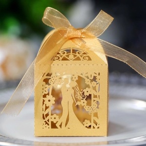 Detailed laser-cut bride and groom silhouette on golden wedding favor box with ribbon