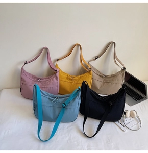 Collection de sacs croissants en nylon en cinq couleurs sur lit blanc avec accessoires