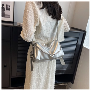 Silver metallic pillow bag with chunky chain detail shown on a model in a white dress