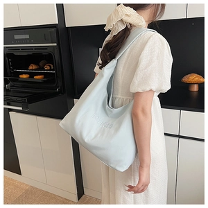 Detail of light blue embroidered tote bag shown worn by a model in a modern kitchen